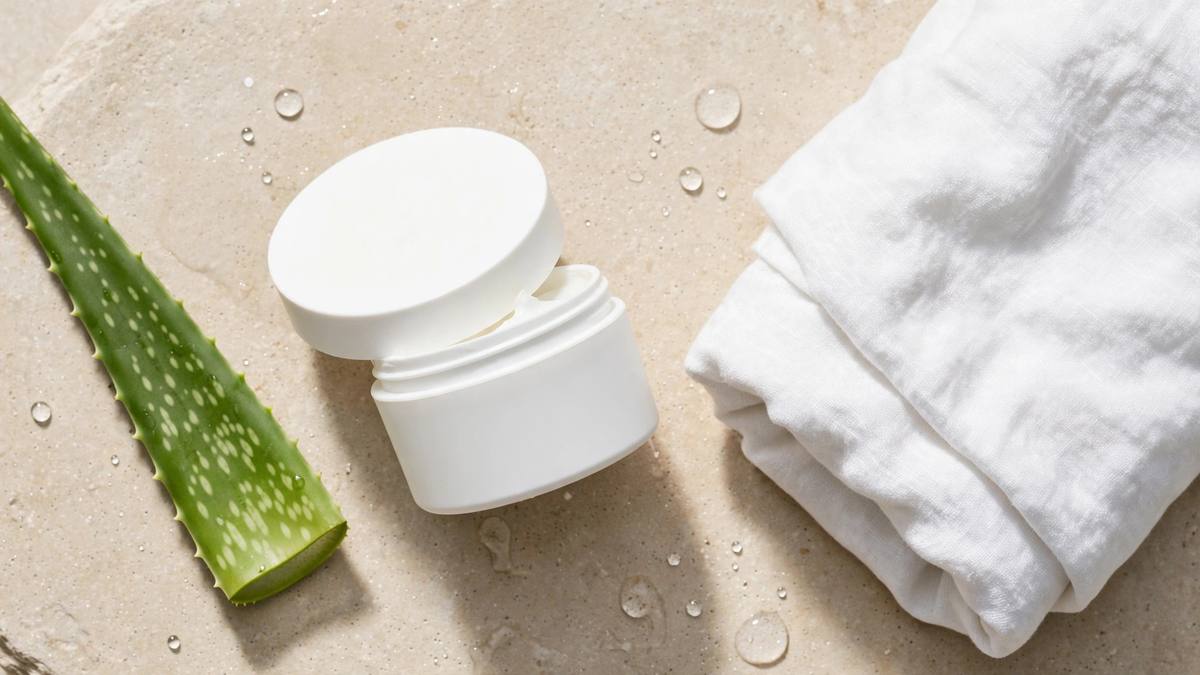 White moisturising cream tub in a minimalist skincare flat lay with aloe leaf and linen towel